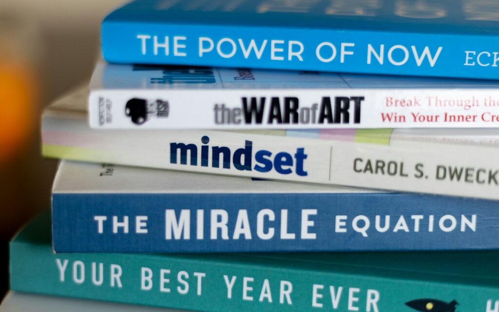 in a desk there are some most famous and bestselling books that are piled up on one by one and they are your best year ever, the miracle equation, mindset, the war of art and the power of now, image from unsplash by seema Miah
