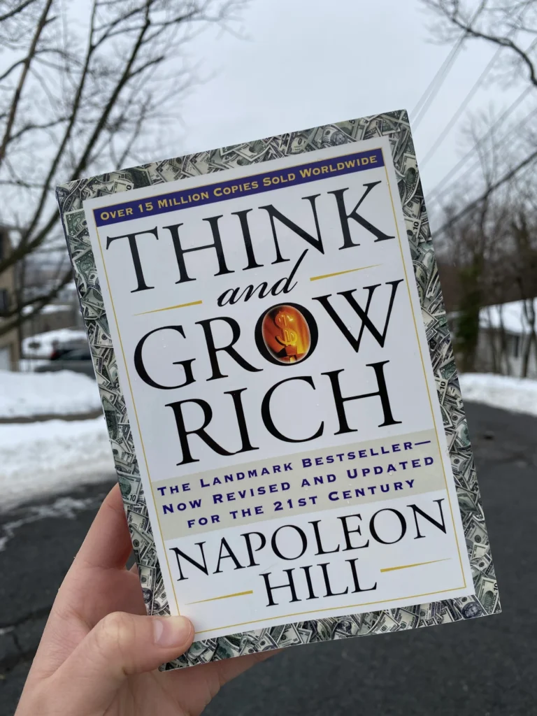 Think and Grow Rich by Napoleon Hill, man's left hand holding the book and the background is winter season and covered with snow.